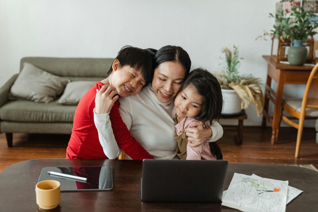 A mother embraces her children while working from home, blending family time with remote work.