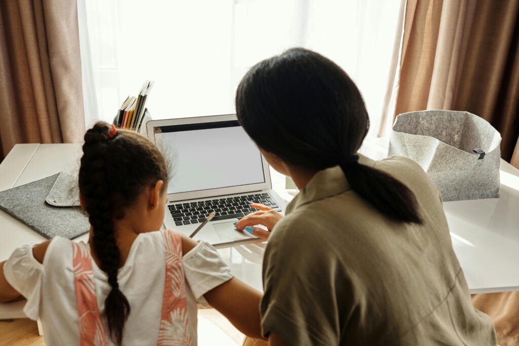 pexels-photo-4260475-4260475 A mother helps her daughter with online learning on a laptop at home, emphasizing family education.